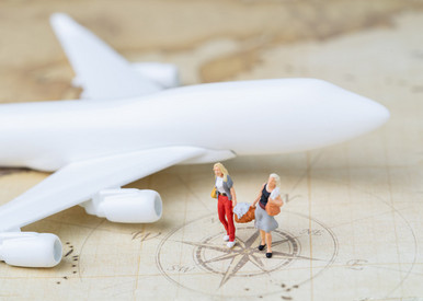 Miniatur-Figurenpaar mit Reisegepäck läuft zusammen vor einem Modellflugzeug auf einer Vintage Weltkarte