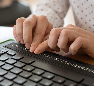 Eine blinde Frau nutzt einen Computer mit Braillezeile