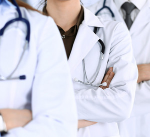 Gruppe von Ärzten steht mit verschränkten Armen hintereinander.