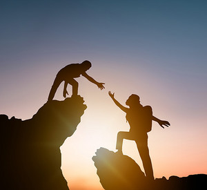Eine Person auf einem Felsen hilft einer 2. Person hinauf