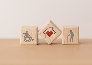 3 Holzblöcke mit Rollstuhlfahrersymbol, rotem Herz in einem Haus und einer Person mit Gehstock