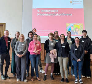 Teilnehmende der Kinderschutzkonferenz stehen in der Alten Mensa der Johannes Gutenberg-Universität Mainz vor einer Präsentation.