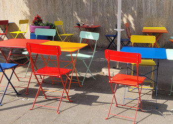 Bunte Tische und Stühle unter einem Sonnenschirm.