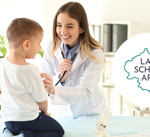 Lächelnde Ärztin prüft mit einem Stethoskop die Gesundheit eines Kind. Recht daneben das Logo "Land schafft Ärzte".