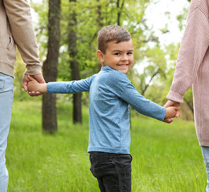 lächelndes Kind an der Hand seiner Eltern im Park