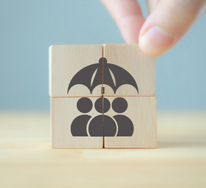 Hand vervollständigt ein Bild mit Figuren unter einem Schirm auf Holzwürfeln