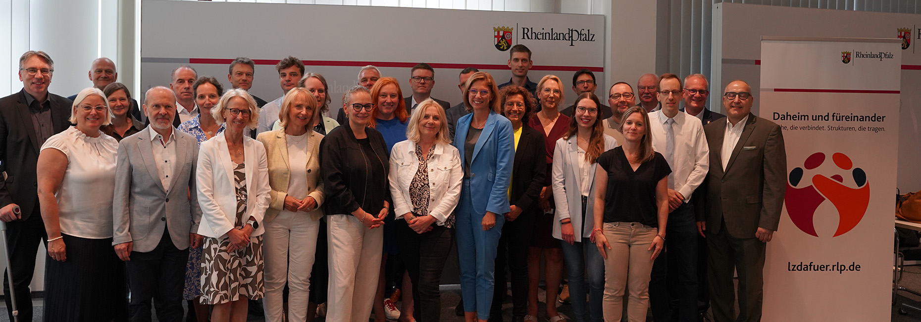 Gruppenfoto, im Hintergrund Roll Up mit dem Logo der Landeszentrale Daheim und füreinander