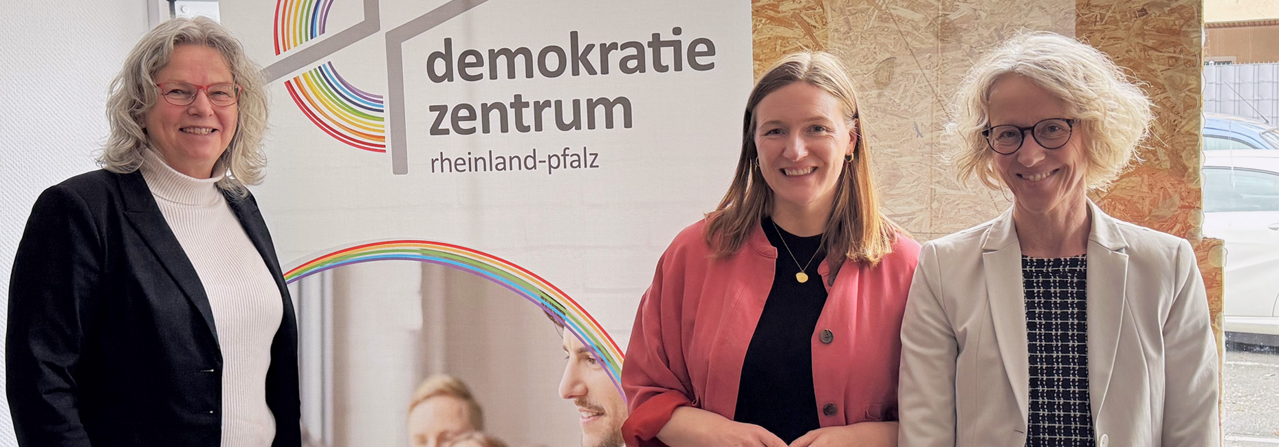Petra Fliedner, vom Demokratiezentrum, Ministerin für Familie, Frauen, Kultur und Integration, Katharina Binz, und die Präsidentin des Landesamtes für Soziales, Jugend und Versorgung, Heike Gorißen-Syrbe, vor einem Roll-Up des Demokratiezentrum Rheinland-Pfalz