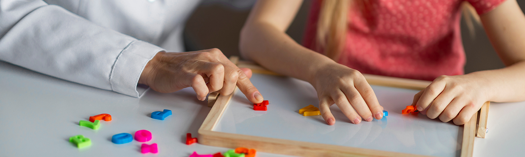 Kids Development Classes. Unrecognizable little girl playing educational games during psychological consultation, female child making words from colorful plastic letters, cropped shot